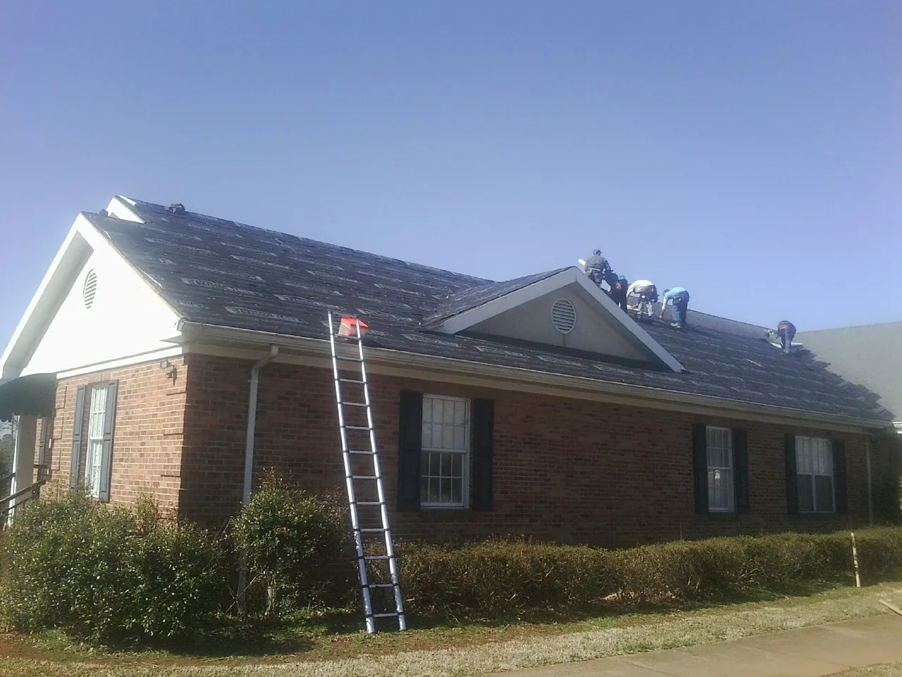 Crew tearing shingles off a brick ranch roof with a ladder set — Metal Roof Repair work by our crew in Trabuco Canyon