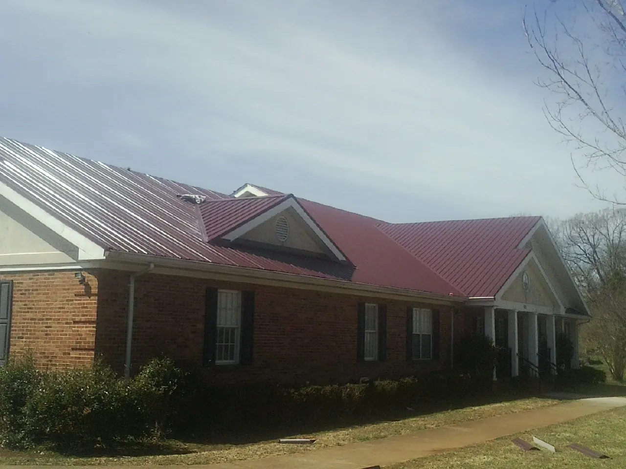 Red metal roof with gabled entries on a long brick building, from a Hail Damage Roof Repair job in Trabuco Canyon
