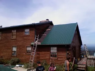 Green metal roof going on a two story log home with ladders set in Trabuco Canyon