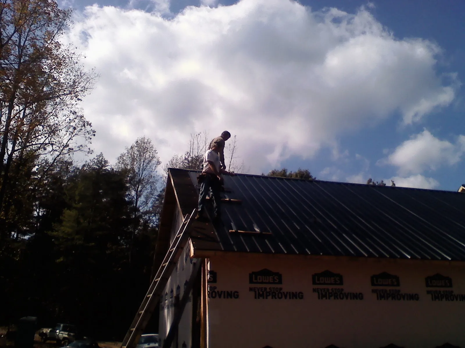 Roofer fastening dark metal panels high against a cloudy sky, from a Roof Inspection job in Trabuco Canyon