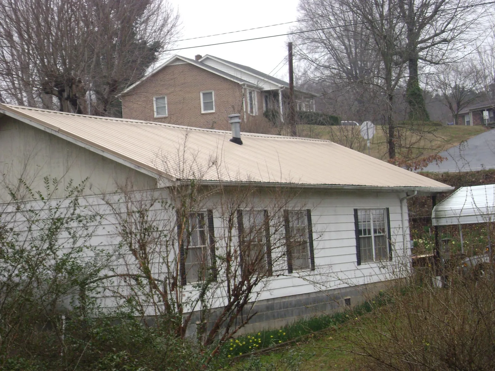 Tan metal roof on a white sided house set into a hillside — Commercial Roofing by Roofing Brothers in Trabuco Canyon